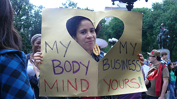 Woman holding sign with heart-shaped cut-out reading: My Body, My Business, Mind Yours