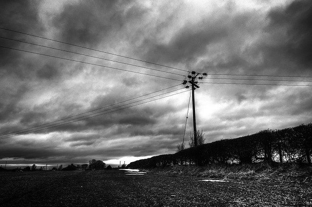 Black-and-white photo of landscape dominated by cloudy sky and lone telephone pole