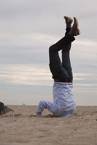 Man doing headstand on beach with head buried in the sand